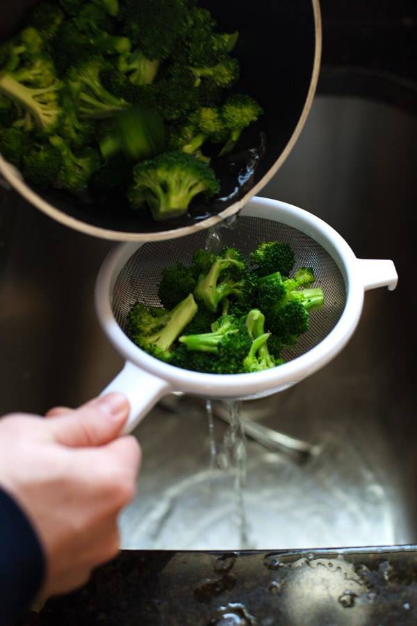 Steamed broccoli being drained in a colander.