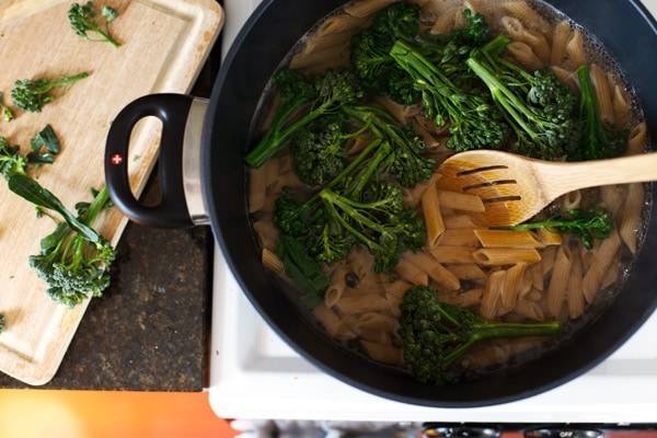 Penne with broccoli in a pan with a wooden spoon.