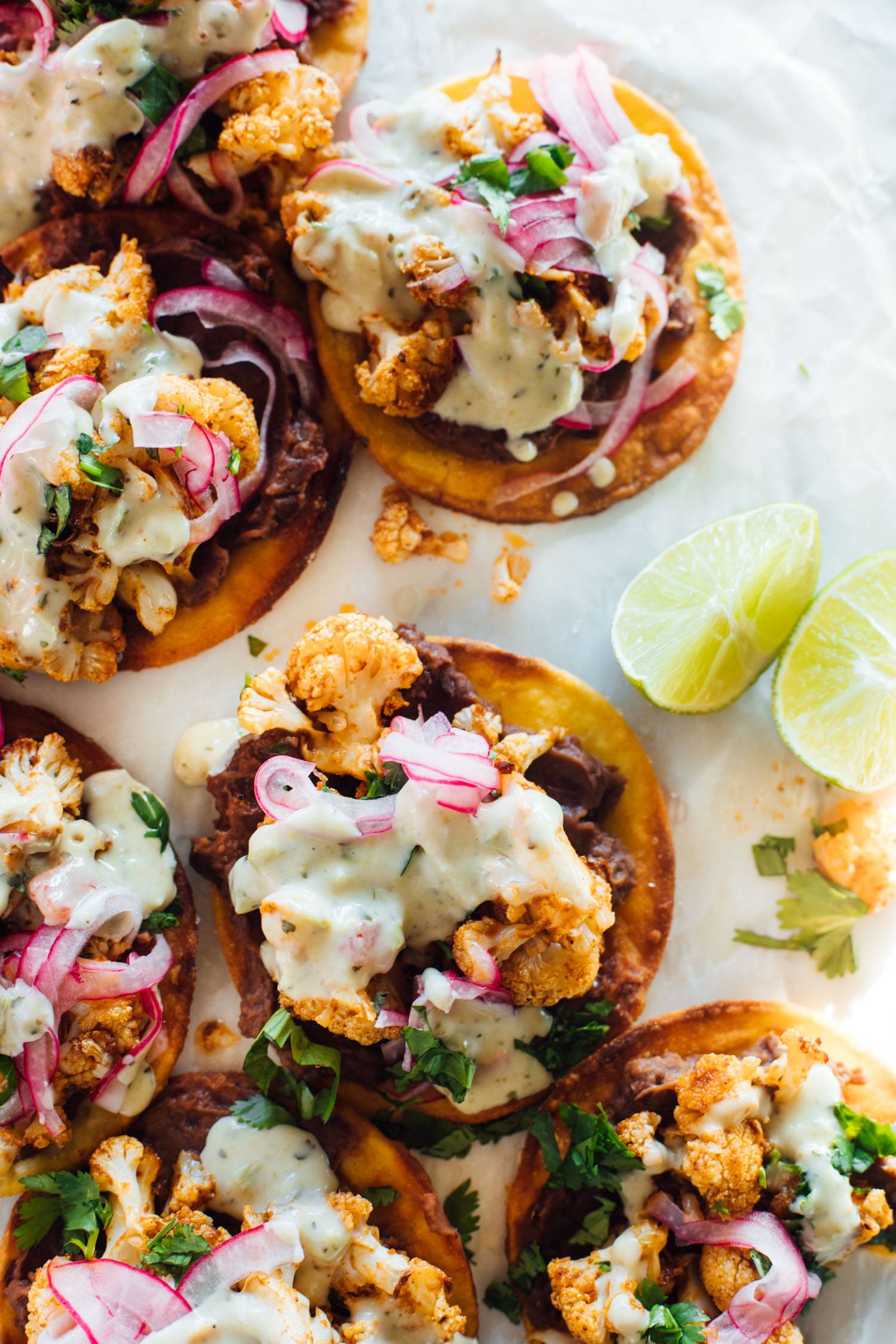 Cauliflower black bean tostadas on parchment paper with pickled onions and queso.