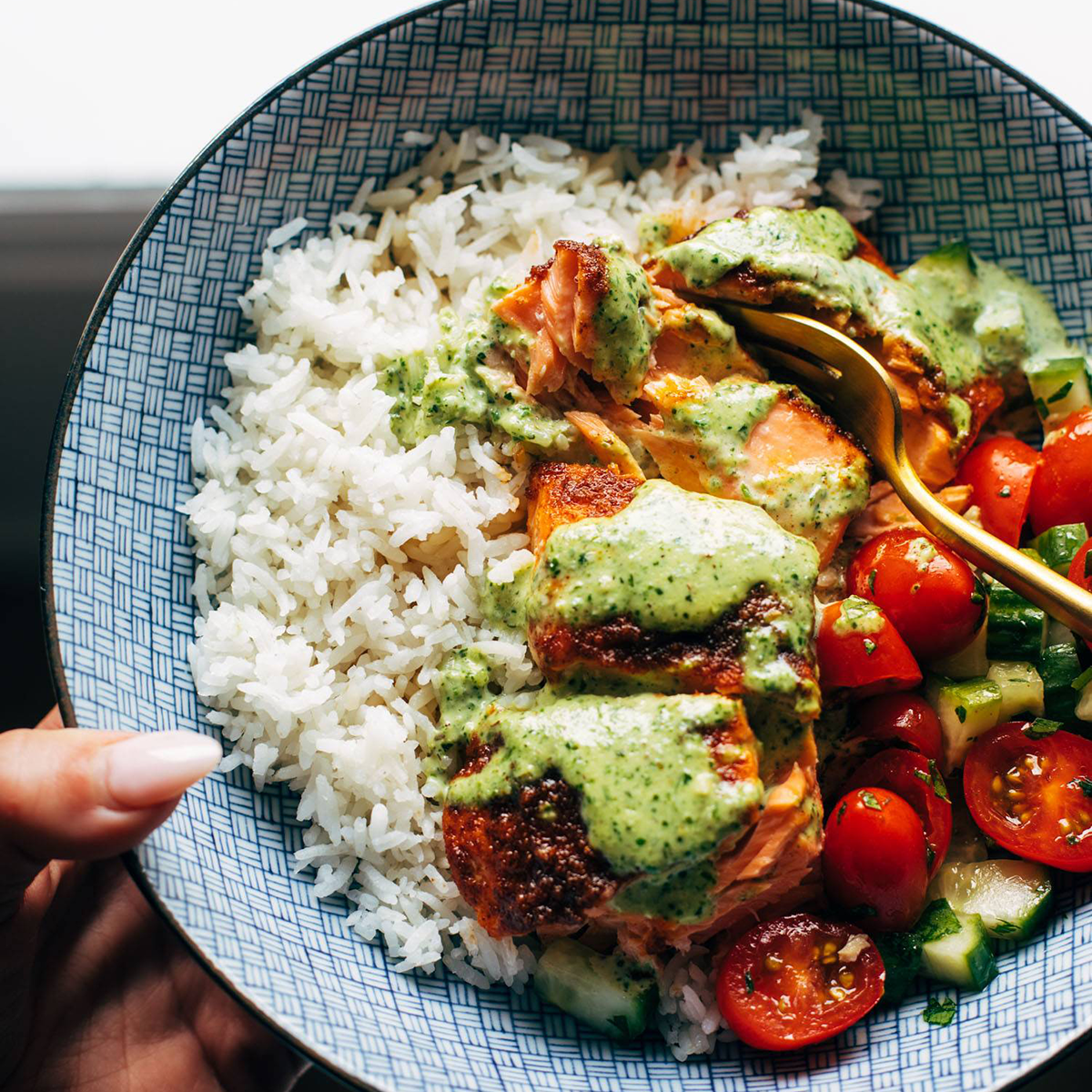 Salmon in a bowl with rice, tomato salad, and a creamy basil sauce on top.