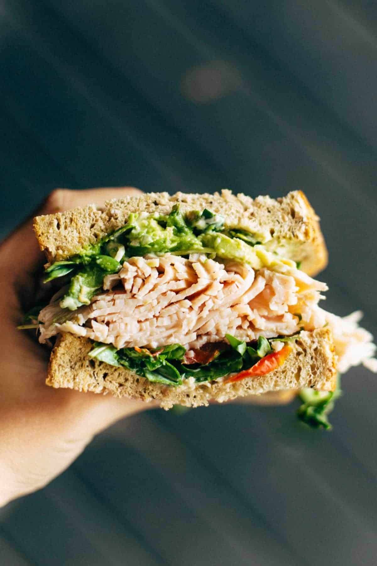 Hand holding a sandwich with lettuce and meat.